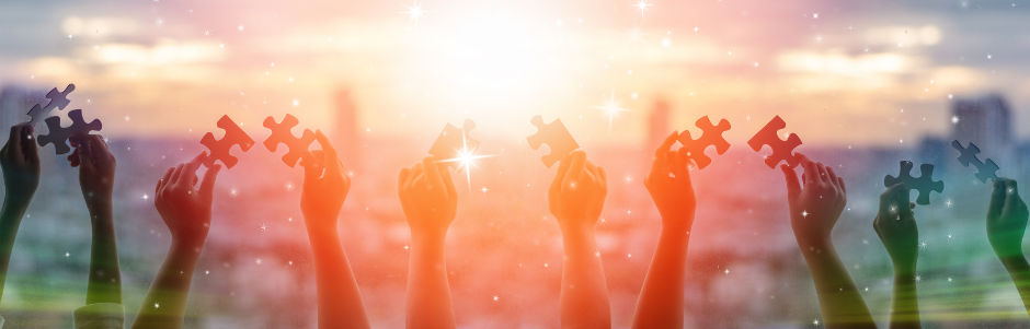 Five pairs of hands holding puzzle pieces up to the setting sun.