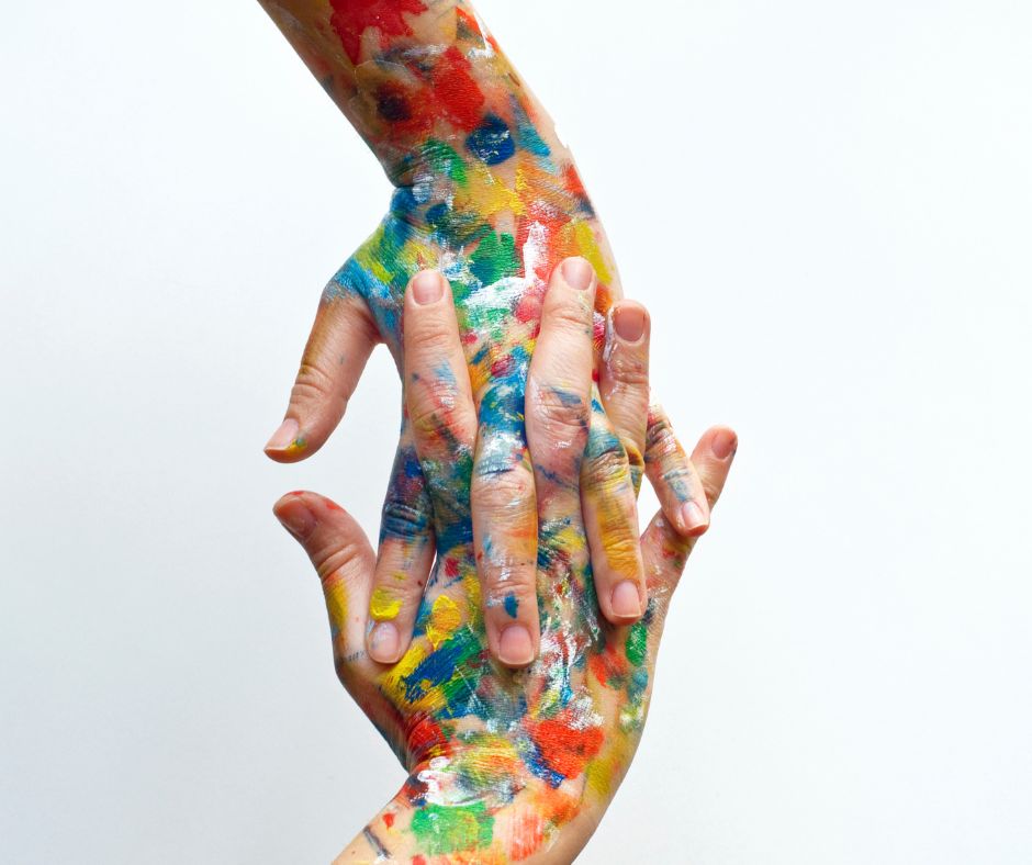 Two hands covered in paint splotches with fingers intertwined.