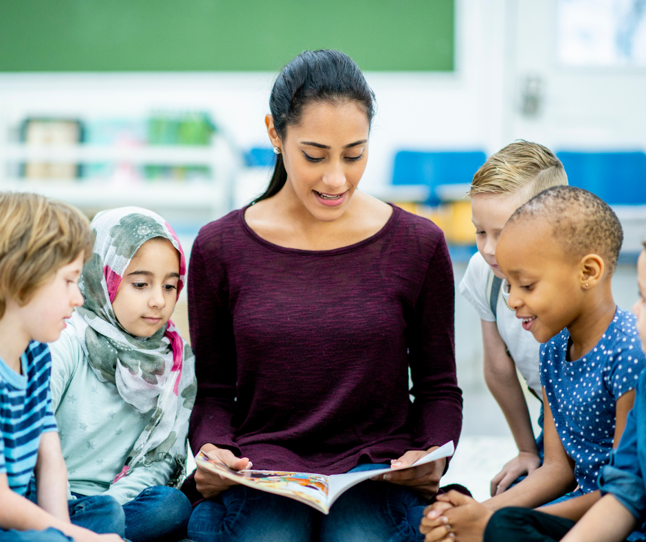 A young woman reading to a group of preschoolers, all sitting on the floor.