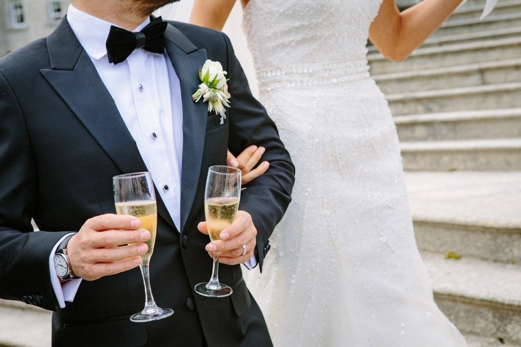 A bride grasping her groom's elbow while he holds two glasses of champagne.
